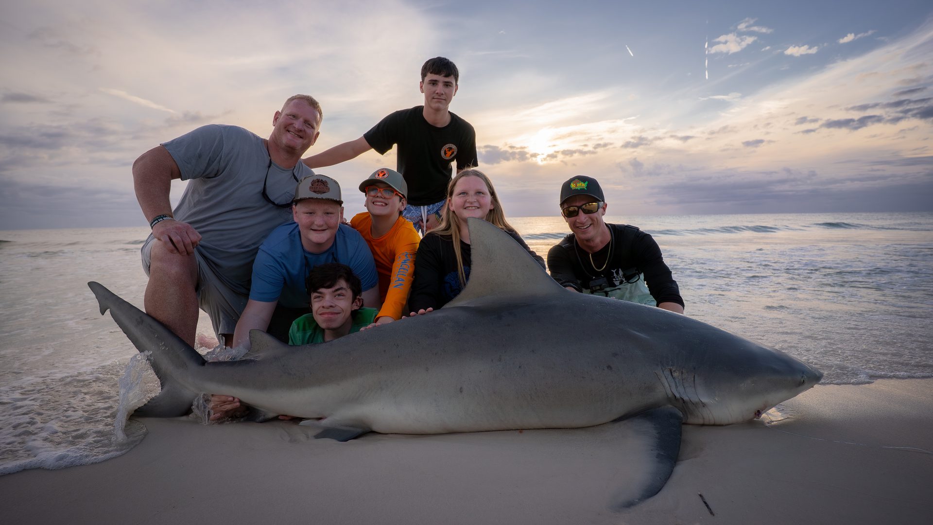 Family group photo with a massive bull shark on the beach at sunset